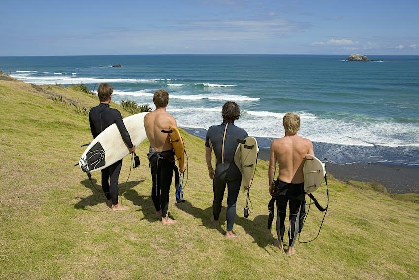 Quatre surfeurs debout sur une falaise surplombant la mer à Auckland Nouvelle-Zélande